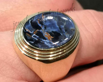 May include: A gold ring with a blue and gold tiger's eye gemstone. The ring has a wide band with multiple grooves.