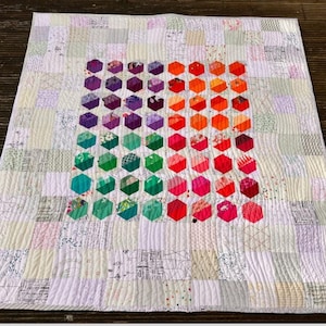 May include: A handmade quilt with a central gradient of colorful, hexagonal patches. The quilt features a patchwork design with a variety of patterned fabrics in white, cream, and pastel hues. The quilt is machine quilted with wavy lines.