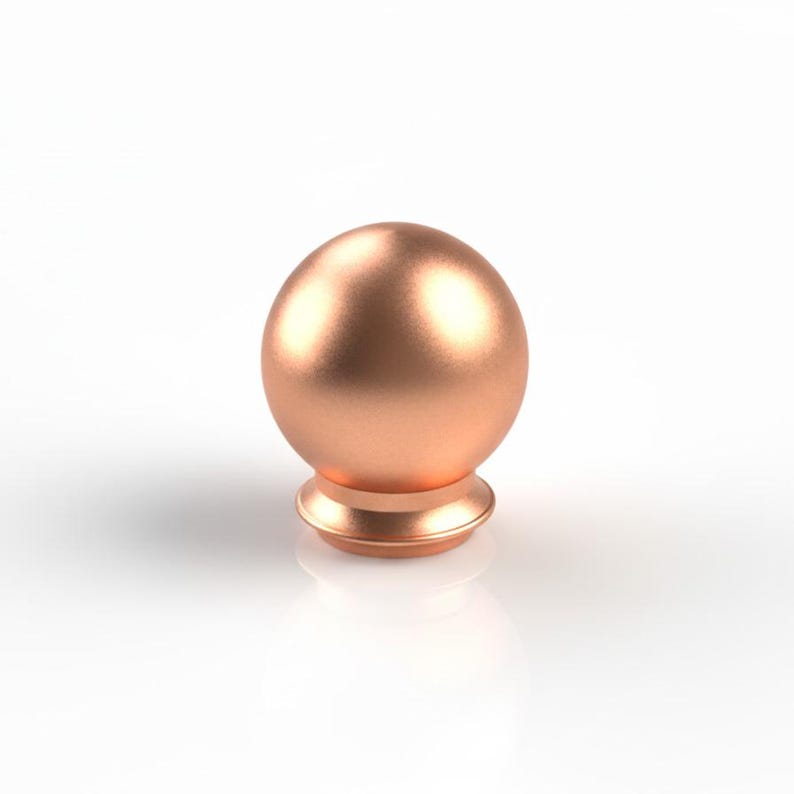 May include: A copper-toned, spherical finial with a rounded base. The finial has a smooth, metallic finish and is designed for decorative purposes. The base has a stepped design, adding visual interest. The object is set against a white background.