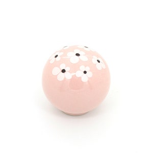 May include: A pink ceramic sphere with a white floral pattern. The flowers have black centers.