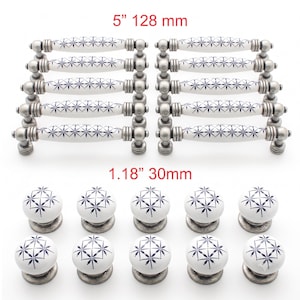 Puede incluir: Diez tiradores de cajón de cerámica blanca con un patrón de estrella azul y herrajes de metal plateado antiguo, de 128 mm de largo, junto con diez pomos de cerámica redondos a juego de 30 mm de diámetro, según indica el texto.