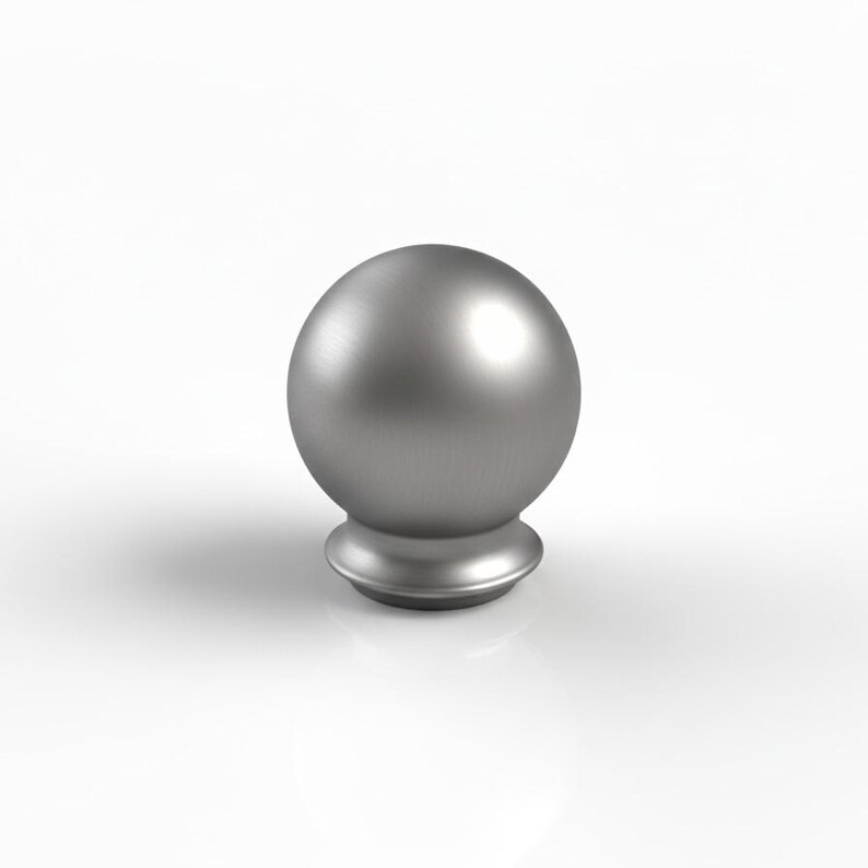 May include: A brushed silver metal finial. It has a spherical top and a decorative base. The finial is designed to be mounted on a rod or pole. The design is simple and modern, with clean lines and a metallic finish.
