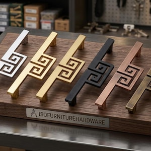 May include: A display of six decorative cabinet pulls in various metallic finishes: silver, gold, black, copper, and bronze. Each pull features a geometric design. The brand name "ISOFURNITUREHARDWARE" is visible on a small label.