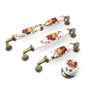 Op de afbeelding: Set van vier keramische kastknoppen met bloemmotieven in tinten rood, oranje en groen. De knoppen hebben een witte achtergrond en een antieke messing basis.