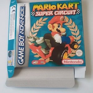 Può includere: Una custodia per cartuccia di gioco Game Boy Advance blu e verde con il testo "Mario Kart Super Circuit" e un'immagine di Mario che guida un kart.