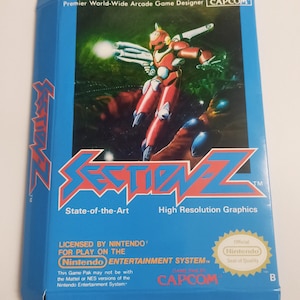 Op de afbeelding: Een blauwe en witte Nintendo Entertainment System-gamebox voor het spel Section Z. De doos toont een rood en wit robotpersonage met een pistool. De tekst op de doos luidt "State-of-the-Art" en "High Resolution Graphics".