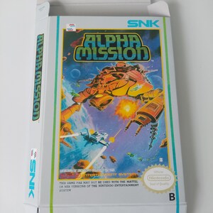 Könnte beinhalten: Eine weiße Schachtel für eine Nintendo Entertainment System-Spielkassette. Die Schachtel hat einen grünen Rand und zeigt ein farbenfrohes Bild eines Raumschiffs, das auf ein größeres Raumschiff schießt. Der Spieltitel lautet "ALPHA MISSION" in großen, fetten Buchstaben. Die Schachtel enthält auch den Text "Licensed by Nintendo for play on the Nintendo Entertainment System." und "This game pak may not be used with the Mattel or NES versions of the Nintendo Entertainment System."