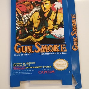 May include: A blue Nintendo Entertainment System game cartridge box for Gun.Smoke. The box features a cowboy character with a gun and a red, white, and blue background. The text "GUN.SMOKE" is in large, bold letters. The box is licensed by Nintendo and made by Capcom.