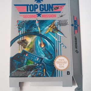 Op de afbeelding: Een grijze en blauwe Nintendo Entertainment System-gamebox voor Top Gun: The Second Mission. De doos toont een straaljager die door de lucht vliegt met een blauwe en witte lucht in de achtergrond. De doos heeft het Konami-logo en het Nintendo-keurmerk.