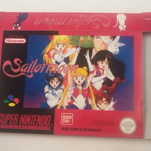 Pode incluir: Uma caixa de jogo Super Nintendo vermelha e branca com os personagens de Sailor Moon. A caixa tem o título "Sailor Moon" em uma fonte estilizada e as palavras "Super Nintendo" em um quadro branco.