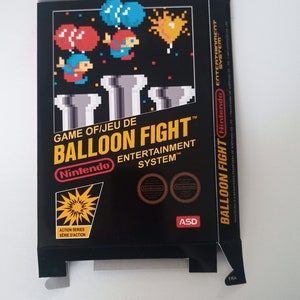 Op de afbeelding: Een zwarte Nintendo Entertainment System-spelcartridge doos met een kleurrijk beeld van een videogamepersonage dat ballonnen vasthoudt. De game heet "Balloon Fight" en is een action-serie game.