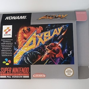 Könnte beinhalten: Eine graue Super Nintendo Entertainment System Spielbox mit einer rosa Klappe. Die Box zeigt ein farbenfrohes Bild eines Raumschiffs und eines Monsters mit dem Text "AXELAY" in großen gelben Buchstaben. Die Box enthält auch den Text "KONAMI" und "PAL VERSION".