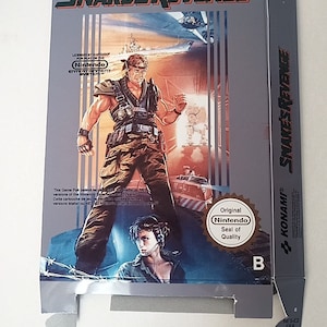 Może przedstawiać: Otwarty karton do gry Nintendo "Snake's Revenge". Grafika na pudełku przedstawia żołnierza w ekwipunku bojowym, futurystyczne miasto i tytuł gry. Pudełko posiada naklejkę "Nintendo Seal of Quality".
