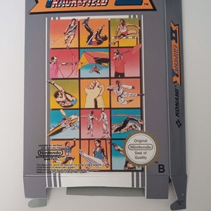 Op de afbeelding: Een grijze Nintendo Entertainment System-gamebox met een kleurrijke illustratie van atleten die in verschillende sporten strijden. De game heet "Track & Field II" en is gelicentieerd door Nintendo. De doos heeft een "Seal of Quality"-sticker van Nintendo.