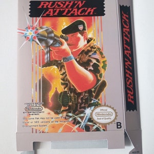 Può includere: Una scatola di gioco Nintendo Entertainment System grigia e bianca con un'immagine di un soldato che tiene una pistola. Il gioco si chiama "Rush'N Attack" ed è concesso in licenza da Nintendo. La scatola ha il sigillo di qualità ufficiale Nintendo.