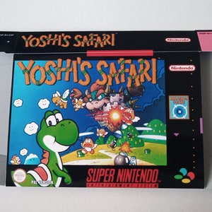 Puede incluir: Una caja de cartucho de juego Super Nintendo negra y verde con el título "Yoshi's Safari" y una imagen de Yoshi en la parte delantera.