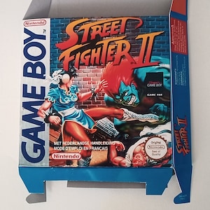 May include: A blue and yellow Game Boy game cartridge box for Street Fighter II. The box features a colourful illustration of two characters fighting. The text on the box reads "Street Fighter II" and "Game Boy Game Pak".