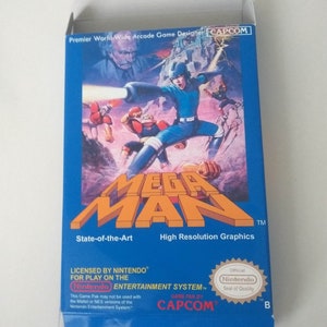 May include: A blue and white Nintendo Entertainment System game cartridge box for Mega Man. The box features a graphic of Mega Man in a blue suit, with a red and white robot in the background. The text "Mega Man" is printed in white on a blue background. The text "State-of-the-Art" and "High Resolution Graphics" are printed in white on a blue background. The text "Licensed by Nintendo for Play on the Nintendo Entertainment System" is printed in white on a blue background. The text "Game Pak by Capcom" is printed in white on a blue background. The text "Official Nintendo Seal of Quality" is printed in white on a red circle with a white border. The text "B" is printed in white on a blue background.