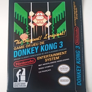 Op de afbeelding: Een zwarte Nintendo Entertainment System-spelcartridge doos voor Donkey Kong 3. De doos heeft een pixelafbeelding van Donkey Kong die aan een liaan hangt. De tekst "The Original! L'original!" staat op de doos gedrukt.