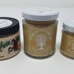 May include: Three glass jars of maple cream, two smaller jars with white lids and one larger jar with a black lid. The jars are labeled "Pure Maple Cream" and "All Natural".