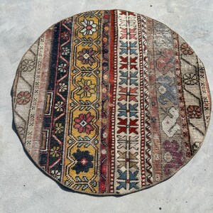 Puede incluir: Una alfombra redonda multicolor con un patrón geométrico. La alfombra tiene tonos de rojo, azul, amarillo y blanco.