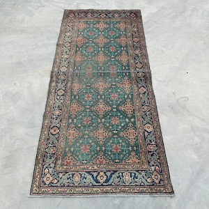 May include: A vintage rug with a green background and intricate floral patterns in shades of red, brown, and blue. The rug has a border with a floral design.