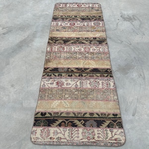 May include: A rectangular, vintage-style rug with a beige, brown, and red color palette. The rug features a striped design with various patterns and textures, creating a unique and aged appearance. The rug is suitable for a hallway or entryway.