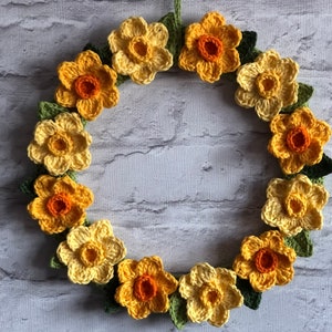 May include: A crocheted wreath featuring yellow and orange daffodils with green leaves.