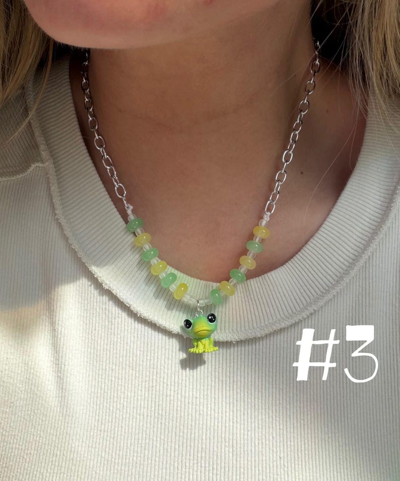 May include: A beaded necklace with a silver chain and a small, green frog pendant. The necklace features yellow and green beads. The number "#3" is visible in the lower right corner.