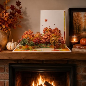 May include: A pop-up greeting card featuring a three-dimensional autumn forest scene with vibrant red, orange, and yellow trees. The card displays a detailed landscape of fall foliage, including scattered leaves on the ground and a single leaf floating above.