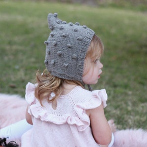 May include: A young child wearing a gray knitted hat with a textured pattern and a pink ruffled dress.