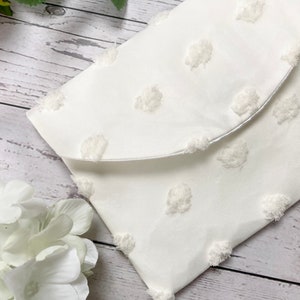 May include: White fabric clutch with a textured polka dot pattern. The clutch has a flap closure.