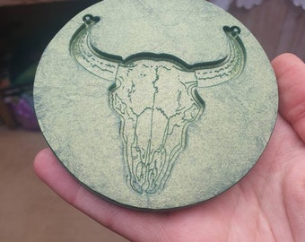 May include: A green circular wooden coaster with a carved bull skull design.