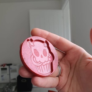 May include: A red circular resin mold with a raised design of a skull wearing a cupcake hat.