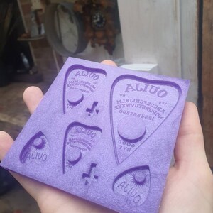 Peut inclure: Moule en silicone violet avec quatre empreintes de planchette de planche Ouija. Chaque planchette porte le mot "ALIUO" et un motif de croissant de lune. Le moule est conçu pour la fabrication d'objets en résine.