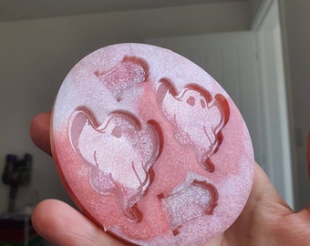 May include: A pink silicone mold with four different shapes: two ghosts, a heart, and a tombstone. The mold is designed for making resin crafts.
