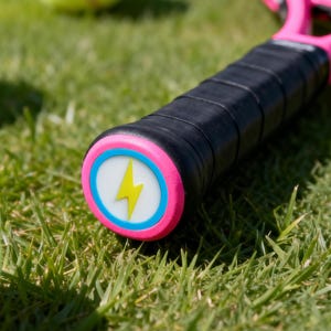 Puede incluir: Una raqueta de tenis rosa con un agarre negro y un diseño de rayo amarillo en el extremo. Varias pelotas de tenis amarillas están esparcidas sobre la hierba verde, creando una escena deportiva.