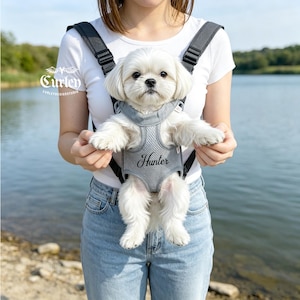 以下が含まれることがあります： 長い毛並みの白い小型犬が、グレーのメッシュ素材のペット用キャリーハーネスに入っています。ハーネスの胸元にはHunterという名前が黒い筆記体で刺繍されています。キャリーには調節可能な黒いストラップとCurleyという文字のロゴが付いています。