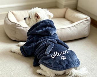 May include: A small white dog wearing a plush navy blue hooded bathrobe with a tie belt. The back of the robe features the embroidered name Maren in white script lettering above a small white paw print graphic, made of soft fleece material.