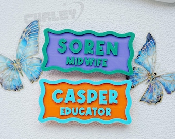 May include: Two name badges with the names "Soren" and "Casper" and their professions, "Midwife" and "Educator". The badges are purple and orange with teal borders and green and teal text. Two blue butterflies with gold accents are on either side.