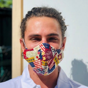 May include: A person wearing a white collared shirt with a face mask. The mask is made of fabric and has a patchwork design of red, white, and blue stars and stripes.