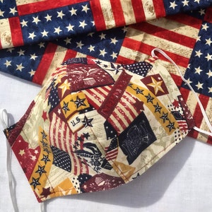 May include: A red, white, and blue fabric face mask with a patriotic design. The mask is made of cotton and has a variety of stars and stripes.