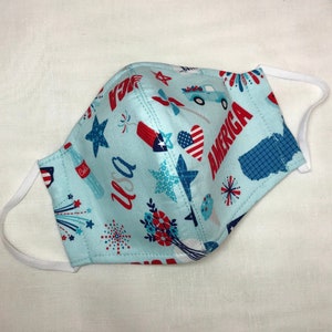 May include: A blue fabric face mask with a white elastic band. The mask has a pattern of red, white, and blue stars, fireworks, hearts, and the words "USA" and "America".