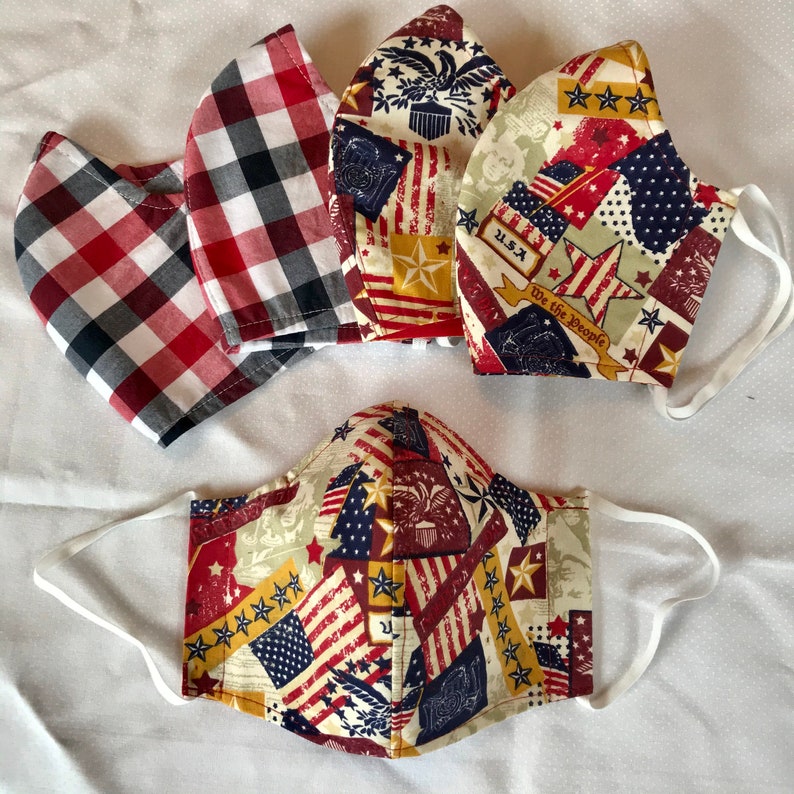 May include: Five fabric face masks with a patriotic theme. The masks feature red, white, and blue stars and stripes, along with the words "U.S.A." and "We the People".