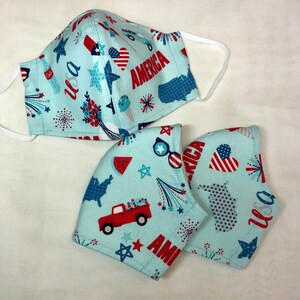 May include: Three blue fabric face masks with red, white, and blue patriotic designs. The masks feature images of fireworks, stars, hearts, trucks, and the word "America".