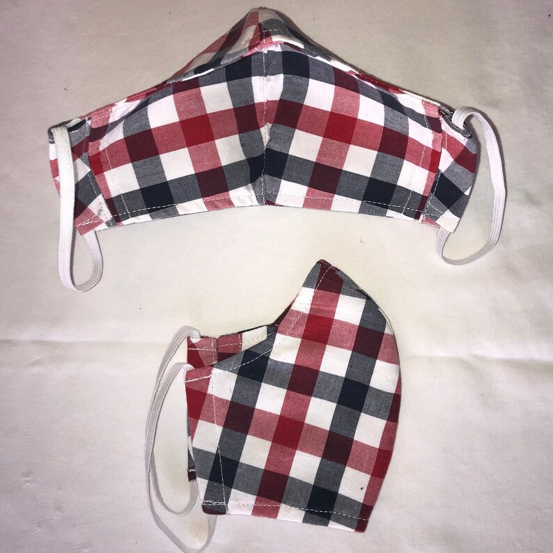 May include: Two red, white, and black plaid face masks with elastic ear loops. The masks are made of fabric and have a checkered pattern.