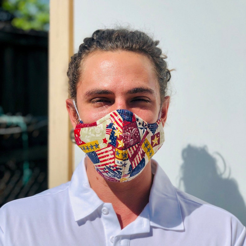 May include: A person wearing a white collared shirt with a face mask. The mask is made of fabric and has a patchwork design of red, white, and blue stars and stripes.