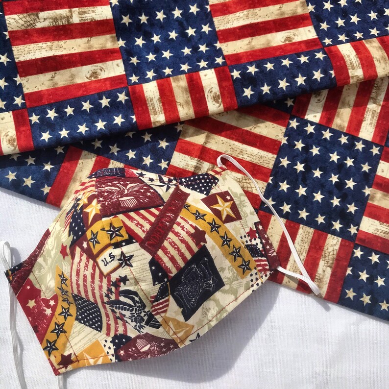 May include: A red, white, and blue fabric face mask with a patriotic design. The mask is made of cotton and has a variety of stars and stripes.