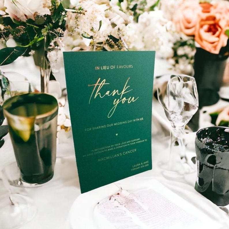 Pode incluir: Um cart&atilde;o de agradecimento de casamento verde escuro com letras douradas. O cart&atilde;o diz "obrigado" e &eacute; rodeado por flores e copos. O texto inclui "Em vez de lembrancinhas" e "Por partilhar o nosso dia de casamento connosco".