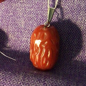 Może przedstawiać: Zestaw biżuterii składający się z naszyjnika i kolczyków. Zestaw zawiera srebrny naszyjnik z czerwoną, owalną zawieszką i pasujące kolczyki. Kolczyki mają zapięcie na haczyk. Biżuteria jest na fioletowym tle.